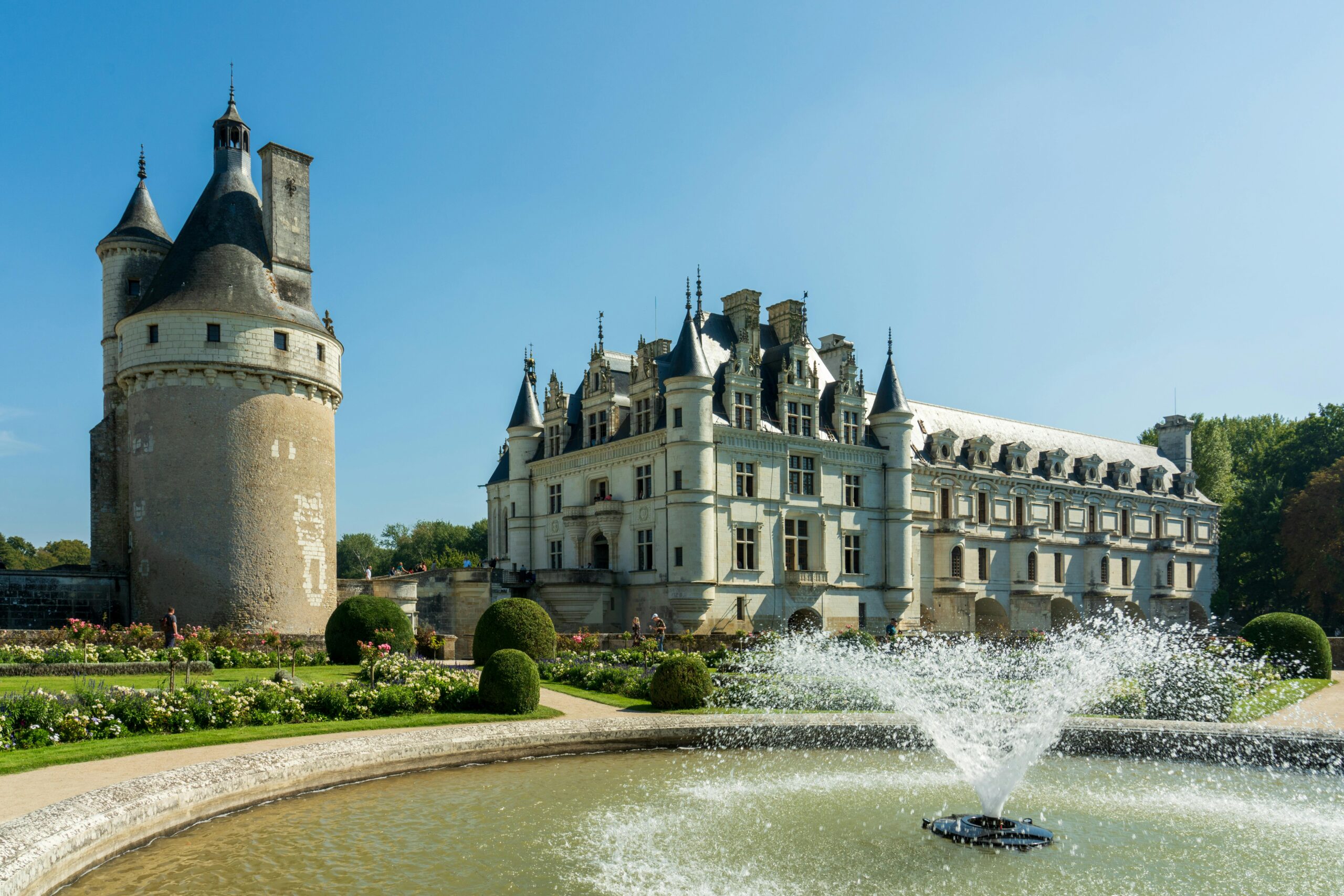 Stunning view of Château de Chenonceau with fountain, showcasing Renaissance architecture in a vibrant garden setting.