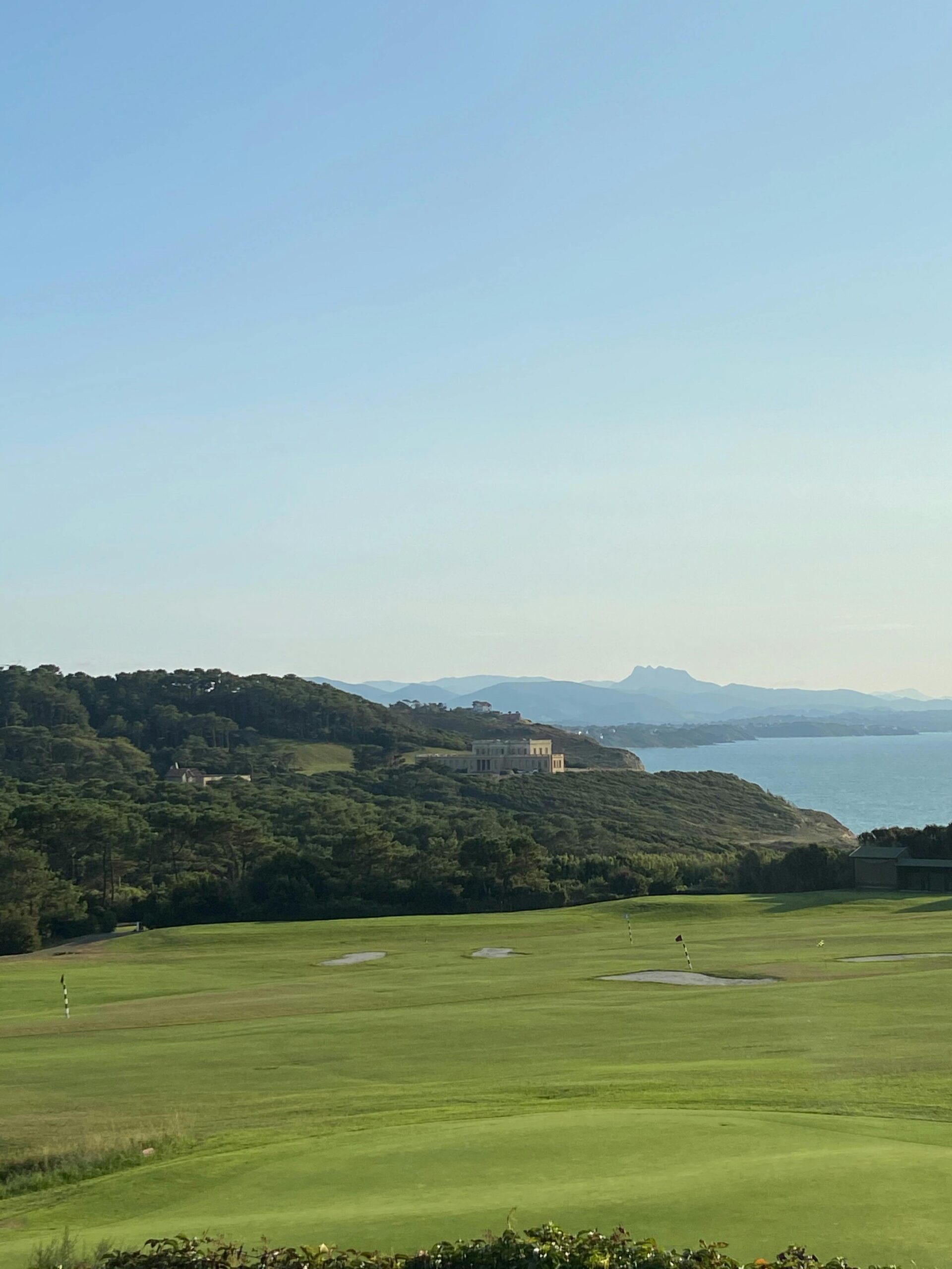 A picturesque view of a golf course by the coast in Biarritz, showcasing lush greenery and serene ocean.